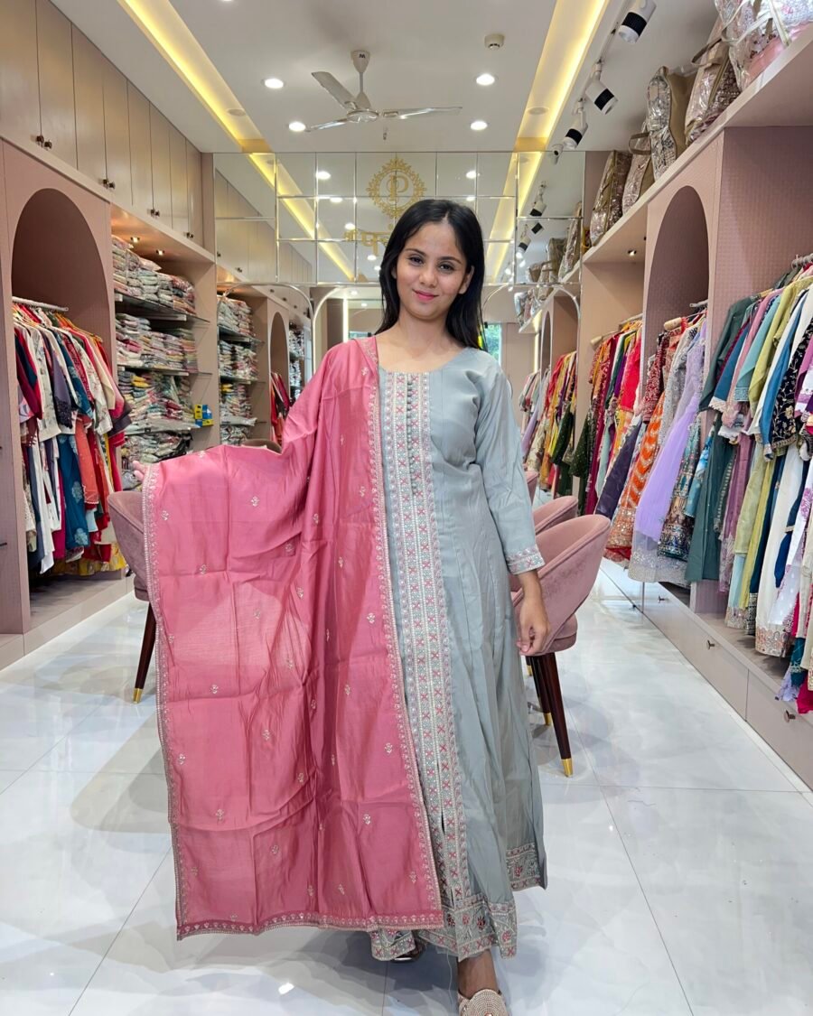 A woman in a boutique posing in a long sage grey kurta with pink embroidery and a large dusty rose dupatta. Text overlay reads "Refined Beauty."