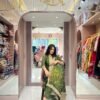 A woman seated in a boutique wearing a bottle green A-line Full kali suit with gold zari embroidery and a matching dupatta.
