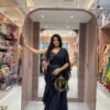 A woman poses inside a luxury ethnic wear boutique leaning against a pillar, wearing a navy blue frill saree and a hand-worked blouse.