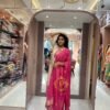 Full-length view of a woman posing in a cream and pink shimmer glass tissue salwar kameez in a well-lit clothing showroom.