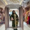 Full-length view of a woman standing in a boutique wearing a bottle green A-line Full kali suit with heavy zari work at the hem.