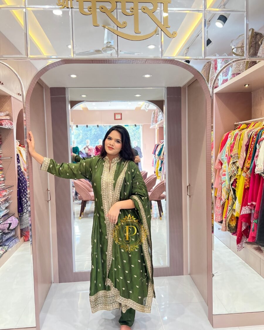 A woman posing against a boutique pillar in a bottle green A-line Full kali suit with shimmering gold zari embroidery.