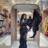 A woman in a navy blue ruffled saree tosses the lightweight pallu into the air, showcasing the movement of the fabric in a clothing store.