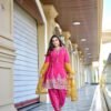 A woman in a hot pink short kurta and Patiala salwar with a mustard yellow dupatta walking down a zigzag patterned balcony.