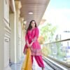 A woman posing gracefully with her hands together, wearing a pink embroidered suit and holding a mustard dupatta to the side.