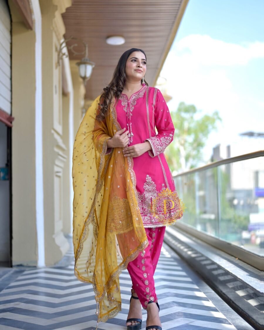 A closer view of a woman in a pink embroidered ethnic suit, highlighting the textures of the fabric and the gold tassels.