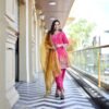 Woman posing with legs crossed at the ankle, wearing a pink Patiala suit and a mustard yellow dupatta.