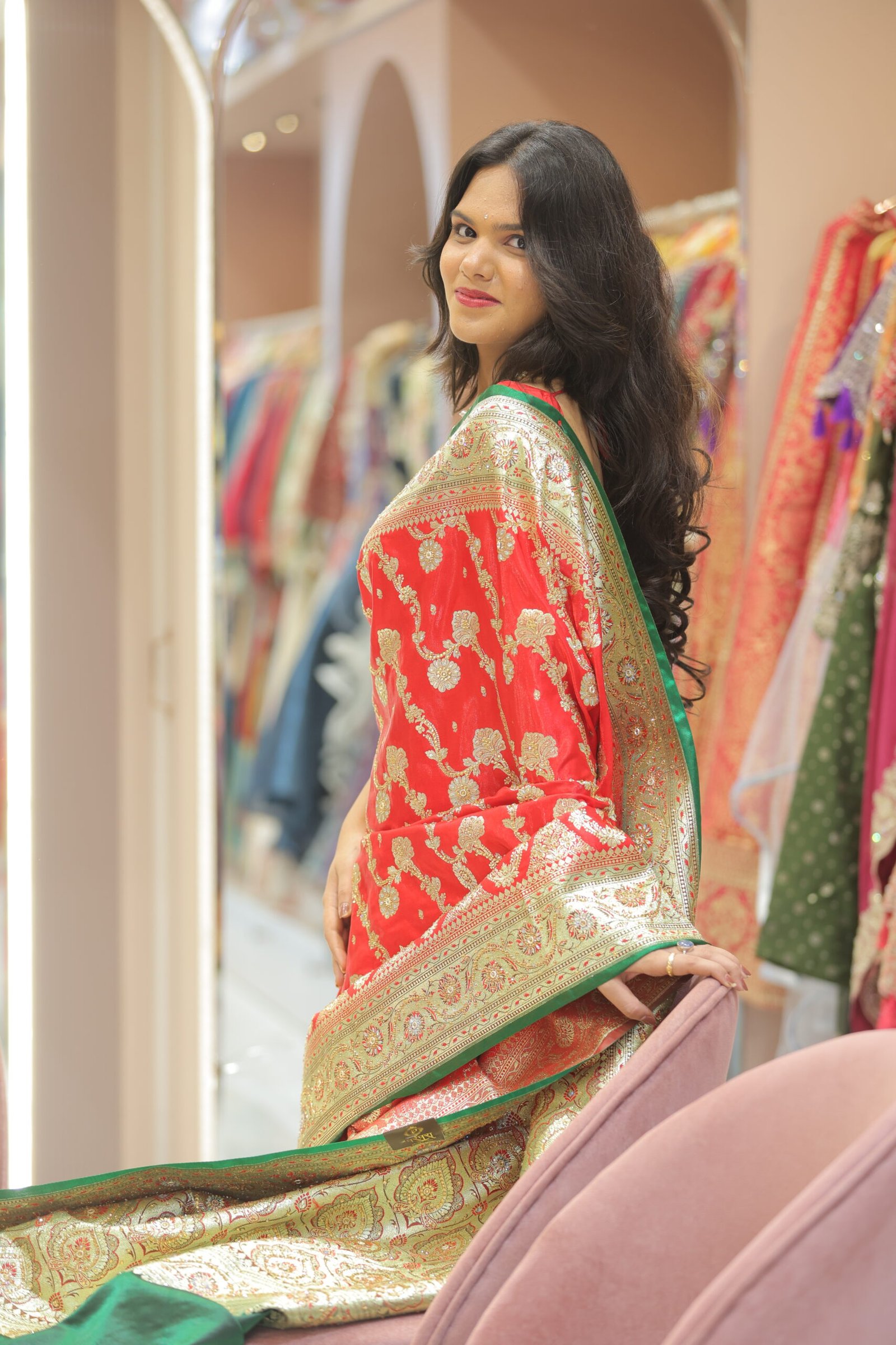 Close-up side profile of a woman wearing a red silk saree with gold floral thread work and a green border.