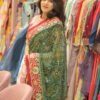 A woman posing in a green and red Bandhani saree surrounded by racks of colorful ethnic clothing.
